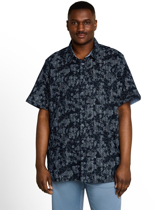 Model draagt een donkerblauw, kort-mouw overhemd met een grillig, lichtblauw patroon. Het overhemd heeft een open kraag.