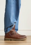 Botte en cuir cognac avec boucle, portée avec un jean.