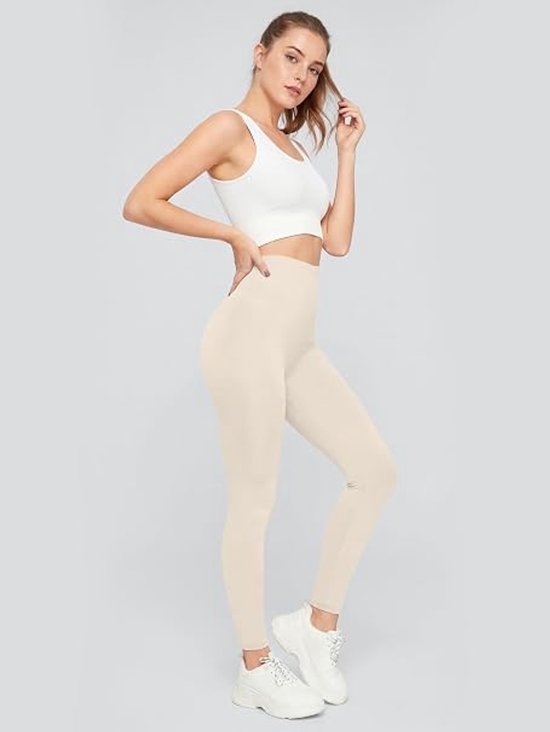 Vrouw poseert in beige legging met hoge taille en witte sportbeha. Strakke pasvorm, enkellengte.