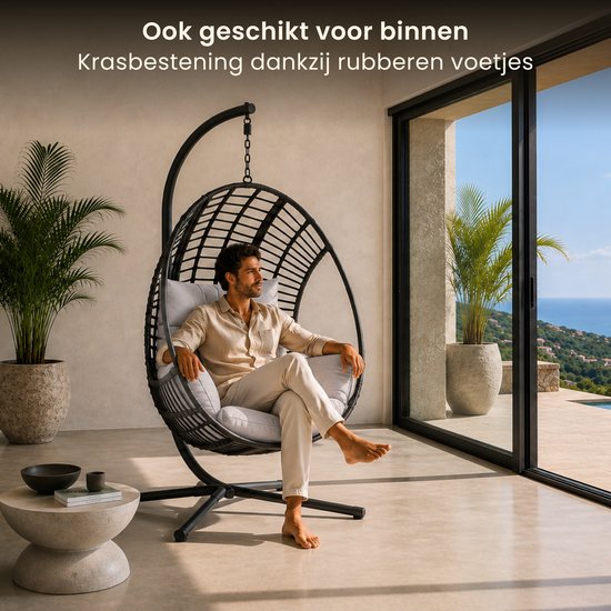 Man ontspant in lichtgrijze Swoods hangstoel in moderne woonkamer met uitzicht op zee.
