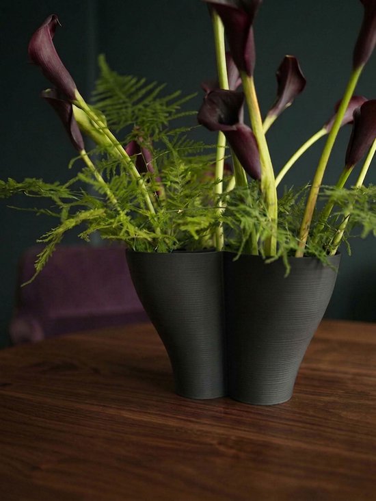 Zwarte, samengevoegde vaas met een golvend patroon, gevuld met donkere calla lelies en varens.