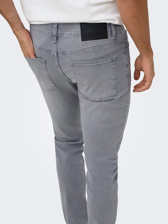 Detail van de achterkant van een grijze slim fit jeans met een zwarte ONLY & SONS-label op de tailleband.