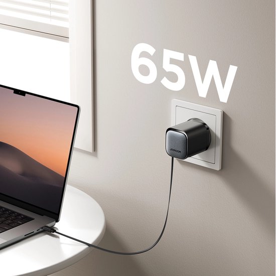 Zwarte 65W-oplader in stopcontact, verbonden met een grijze laptop via een kabel.
