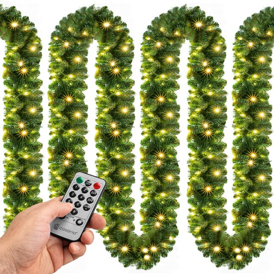 Hand met afstandsbediening voor de Casaria kerstguirlande met warmwitte LED-lampjes op een groene slinger.
