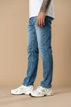 Zijaanzicht van de blauwe rechte jeans met witte sneakers.