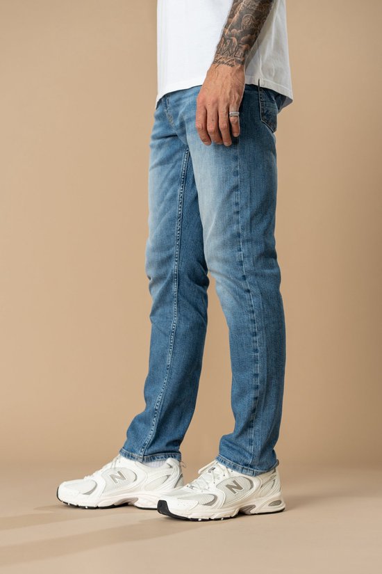Zijaanzicht van de blauwe rechte jeans met witte sneakers.