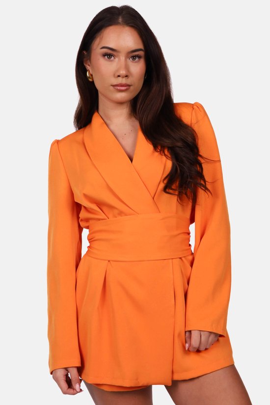 Model draagt een oranje blazerjumpsuit met reverskraag, pofmouwen en een ceintuur in de taille.