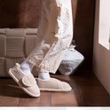 Model draagt beige pluche pantoffels met klittenbandsluiting, gecombineerd met een gestippelde broek.