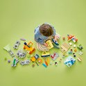 Kind van bovenaf gezien, zittend op een groene ondergrond, omringd door losse LEGO Duplo treinonderdelen.