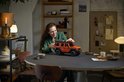Een vrouw controleert de oranje LEGO Technic Mercedes-Benz G 500 op een tafel.