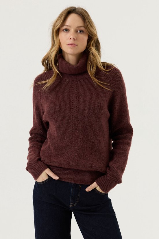 Model met bordeauxrode Garcia coltrui en donkerblauwe jeans, handen in de zakken.