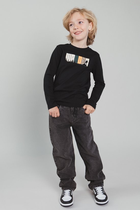 Jongen draagt een zwarte longsleeve met 'WANDER' opdruk, grijze jeans en sneakers.