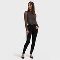 Model draagt bruine mesh top met hartjesprint en zwarte skinny jeans, staand op hoge hakken.