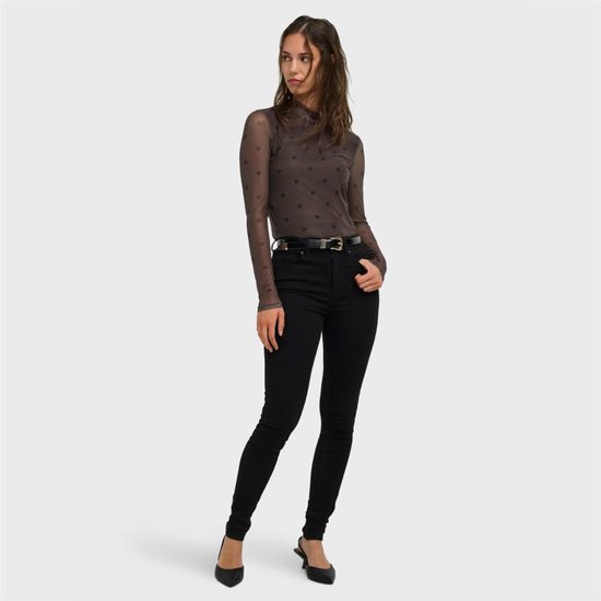 Model draagt bruine mesh top met hartjesprint en zwarte skinny jeans, staand op hoge hakken.