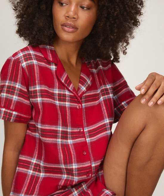 Model draagt een rode pyjamaset met ruitpatroon en knoopsluiting.