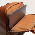 Bruine leren rugzak met een geopend vak waarin een laptop is opgeborgen.
