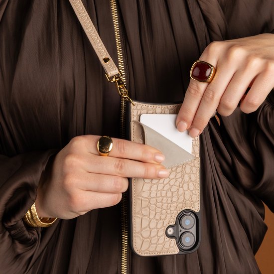 Beige croco-print telefoonhoesje met pashouder en goudkleurige ketting, gedragen over een bruine blouse.