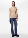 Model in een beige hemdje met kanten rand en blauwe jeans, staand op een witte achtergrond.