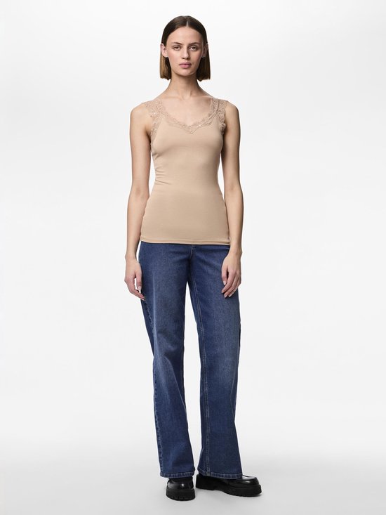 Model in een beige hemdje met kanten rand en blauwe jeans, staand op een witte achtergrond.