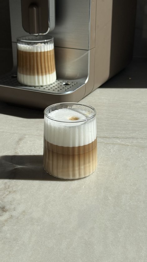Deux verres côtelés, remplis de café stratifié avec de la mousse de lait, à côté d'une machine à café.