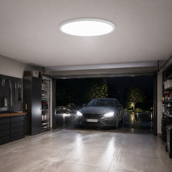 Een ronde, witte LED-plafondlamp verlicht een garage waarin een auto 's nachts de oprit oprijdt.