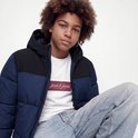 Model in een zittende houding draagt een marineblauwe en zwarte jas over een wit 'Jack & Jones' T-shirt.