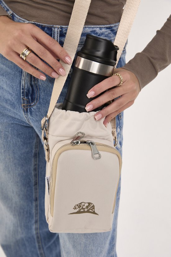 Beige crossbody tas met een ritsvak aan de voorkant met een berenlogo. Een zwarte thermosfles wordt in het geïsoleerde hoofdvak geplaatst.