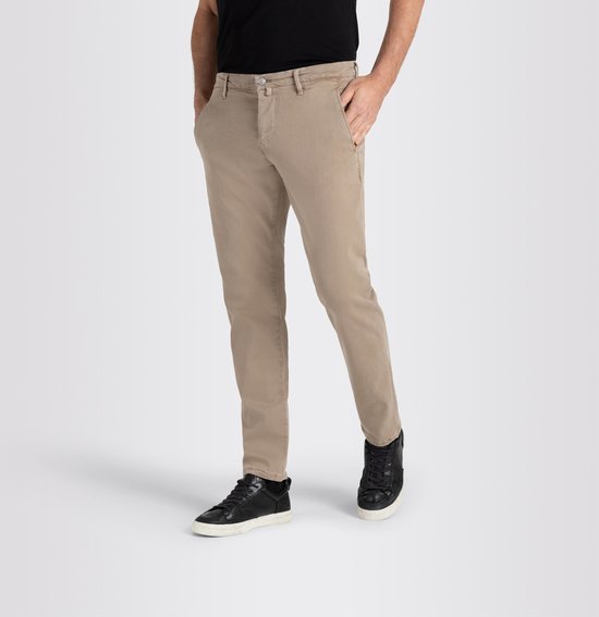 Man in beige chino broek met zwarte sneakers en zwarte T-shirt, handen in zakken.