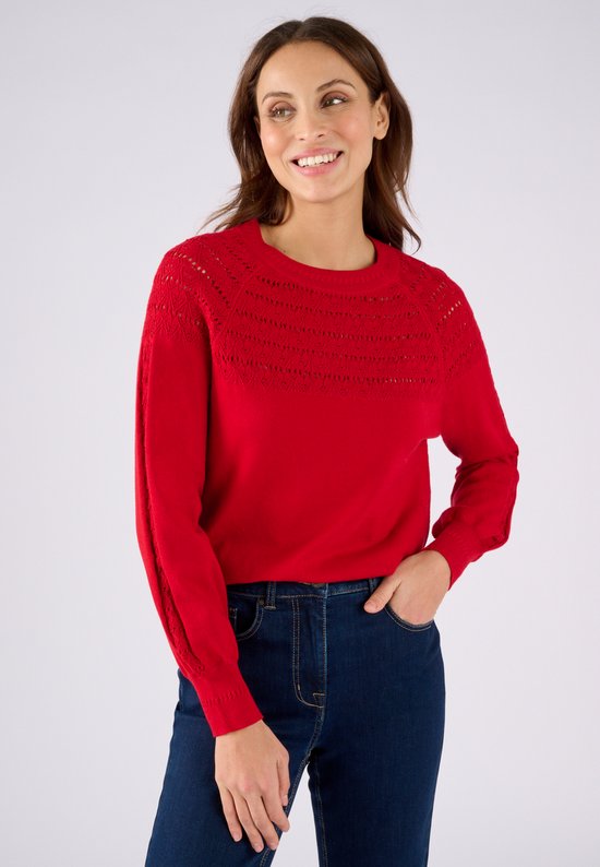 Femme portant un pull rouge en maille, avec détails ajourés sur les épaules.