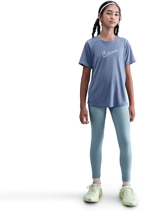 Volledig beeld van een meisje met gevlochten haar, draagt een blauw Nike t-shirt met witte swoosh en lichtblauwe legging.