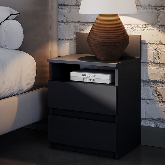 Une table de nuit noire à côté d'un lit, avec deux tiroirs et une étagère. Une lampe est posée dessus.