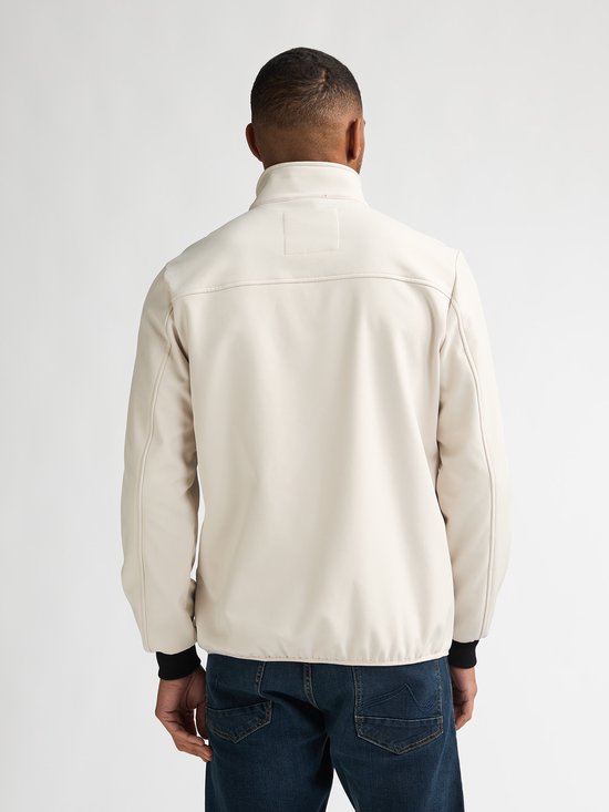Man met de rug naar de camera in een effen beige jas met zwarte boorden aan mouwen en vest.