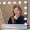 Vrouw met blond haar gebruikt make-up in een spiegel met verlichting.