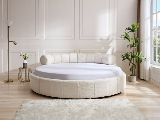 Chique ronde bed in een woonkamer, met beige teddy-stof, gebogen hoofdbord en witte lakens.