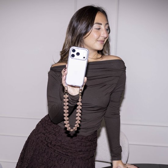 Vrouw met bruine off-shoulder top en bruine kanten rok, houdt een doorzichtige telefoonhoes met een donkerbruin koord van hartjes vast.