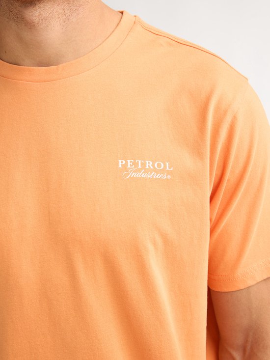 Model draagt een oranje t-shirt met "PETROL Industries" op de borst.