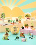 Miniatuur tuin scène met verschillende plantjes in potjes, een kruiwagen, gieter en zakjes potgrond.