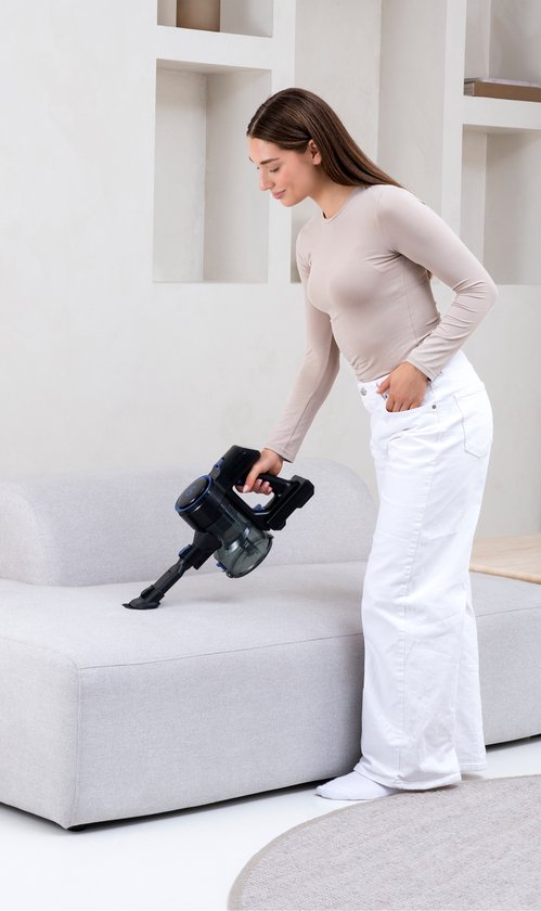 Vrouw in beige top en witte broek zuigt bank schoon met zwart mondstuk.