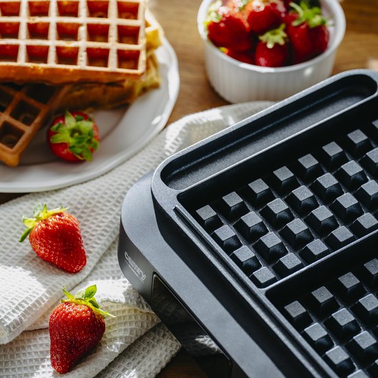 Close-up van de binnenkant van een zwart wafelijzer met wafelvormige vakken.