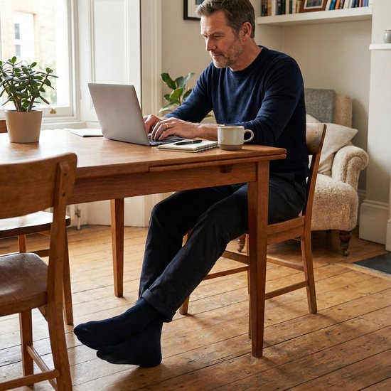 Man op donkerblauw pakbroek en sokken werkt op laptop.