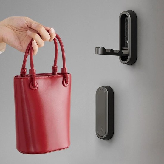 Hand houdt een rode tas, bij een zwarte, opklapbare wandhaak en een gesloten haak.