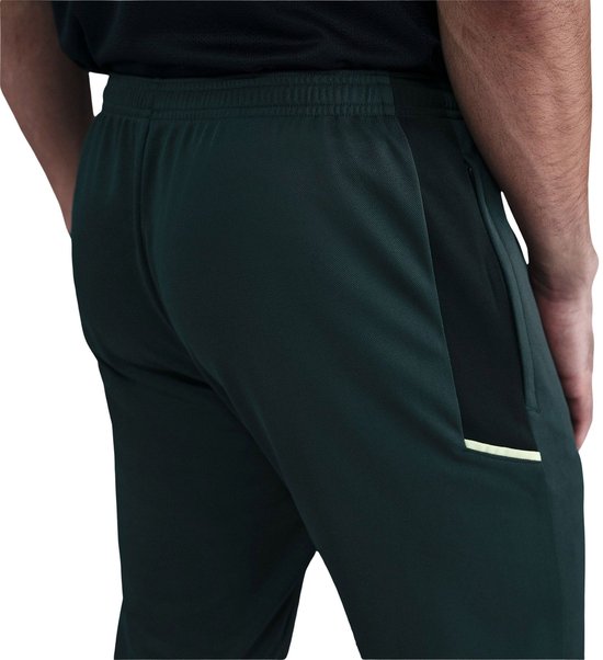 Donkergroene Nike trainingsbroek met witte swoosh en gele accenten.