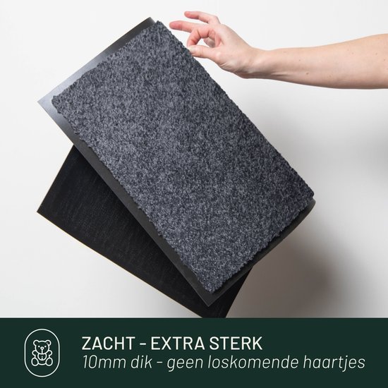 Grijze deurmat wordt opgetild door een hand, onderkant zichtbaar. Tekst 'Zacht - extra sterk'.
