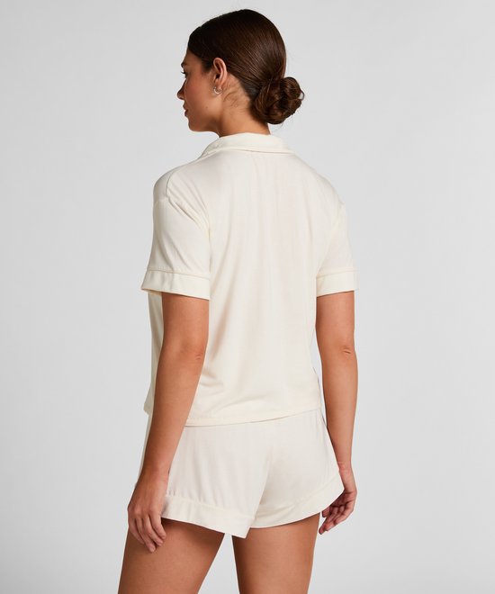 Model met de rug naar de camera, draagt een roomwitte pyjamashort en een bijpassend pyjamashirt met korte mouwen.
