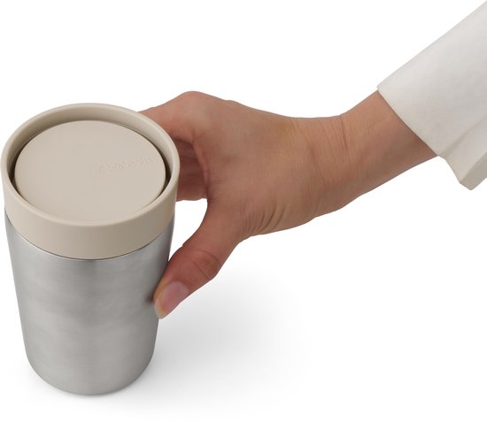 Hand houdt een zilverkleurige thermosbeker vast met zandkleurig deksel.