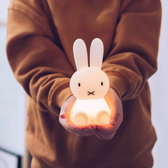Handen in een warme, bruine trui houden een verlicht, wit Miffy-lampje vast.