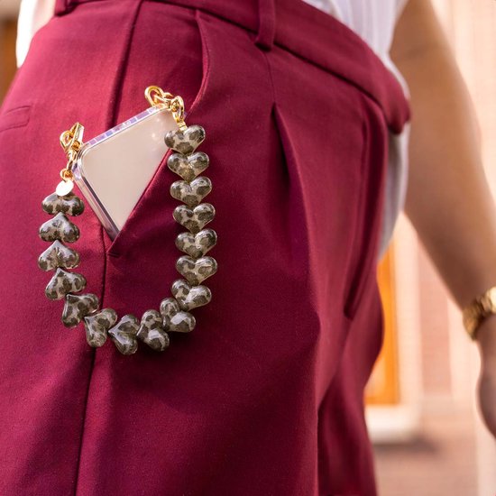Gouden schakels van een telefoonketting met bruine hartjes met luipaardprint, in de zak van een rode broek.