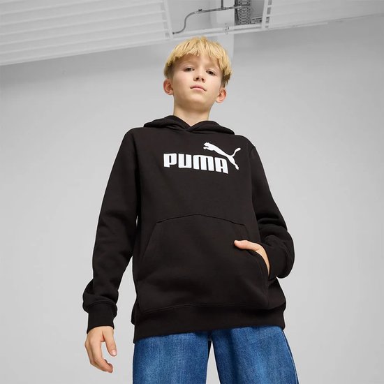 Jongen draagt een zwarte PUMA hoodie en spijkerbroek, poseert met de hand in de zak.