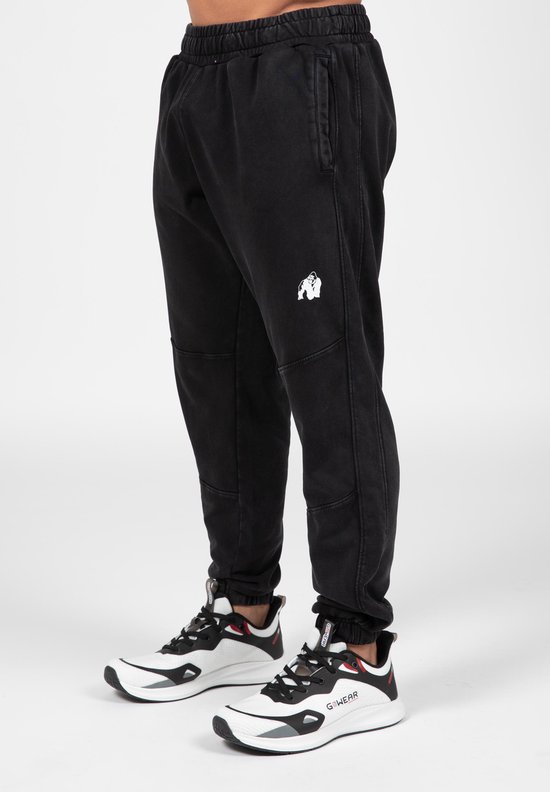 Man draagt zwarte joggingbroek met witte gorilla opdruk en witte sneakers.