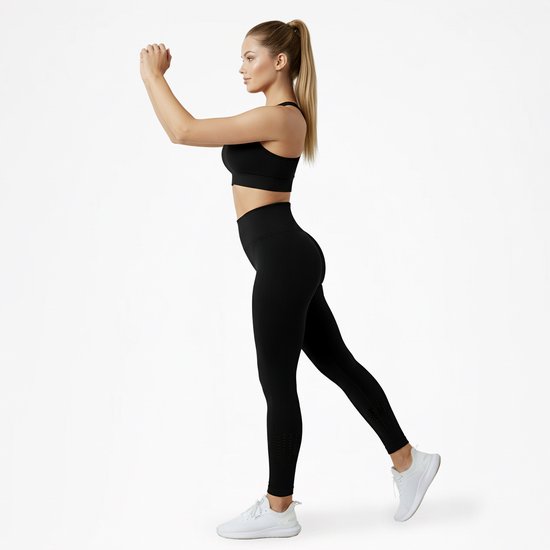 Vrouw, zijaanzicht, draagt een zwarte sportbeha en zwarte legging met hoge taille en perforaties.